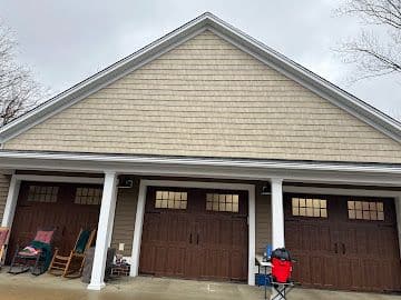 Three-bay garage with cedar shake siding, white columns and wood-look carriage doors