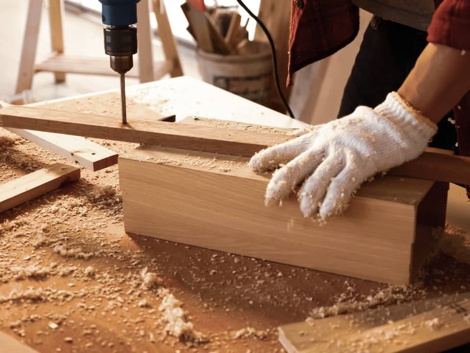 Carpenter drilling a hardwood joint on a workbench covered in sawdust