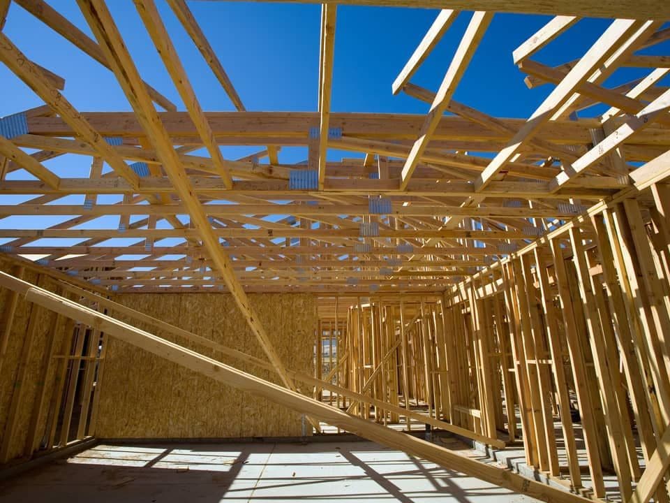 New house framing with roof trusses and stud walls under a clear sky